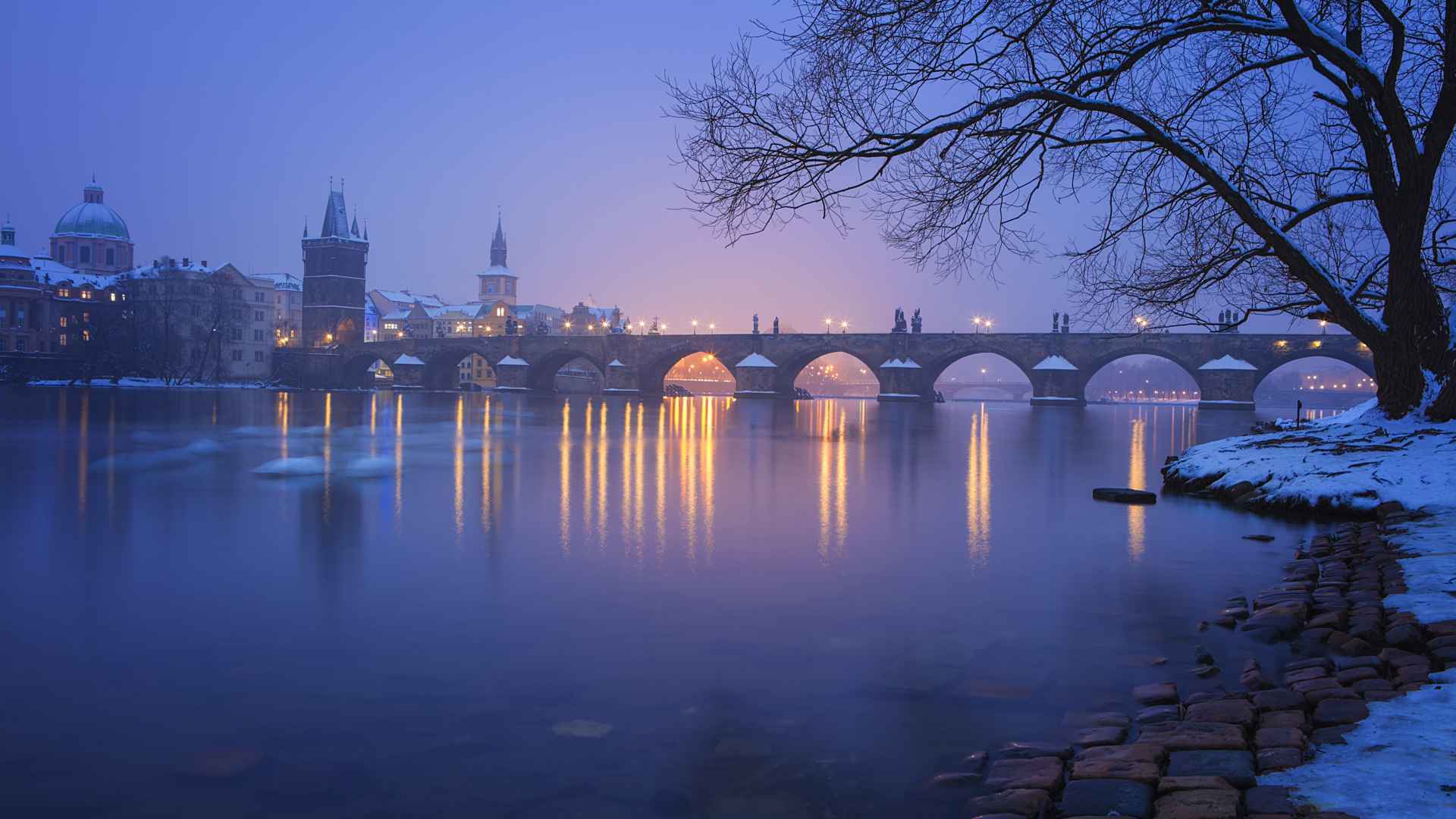 Η Charles Bridge στην Πράγα το χειμώνα με μπλε ουρανό και αντανακλάσεις στον ποταμό Μολδάβα